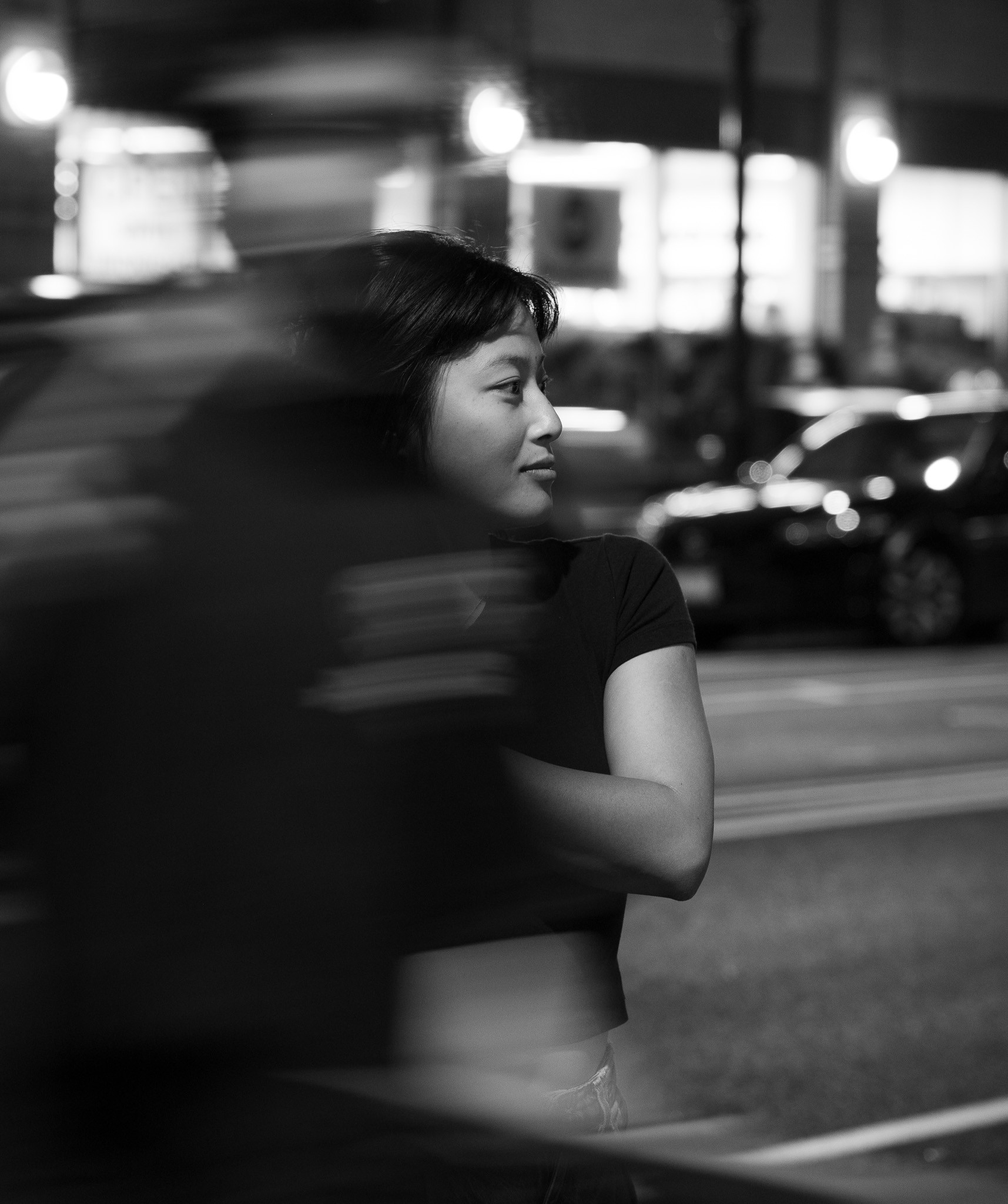 A young woman glancing over her shoulder on a city street at night, a blur of motion sweeping past in front of her